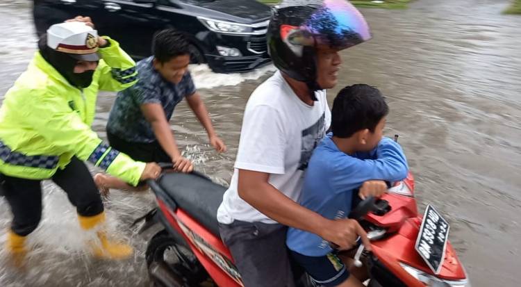 Ditengah Hujan dan Banjir, Kasat Lantas Polres Dumai Dorong Motor dan Seberangkan Pelajar SD